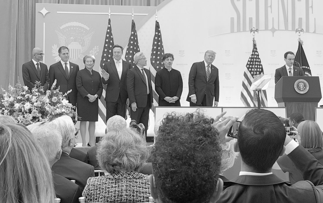 Black-and-white photograph of the recipients of the National Medal of Technology and Innovation standing on stage beside the President, under the word Science, while the audience in the foreground photographs them.
